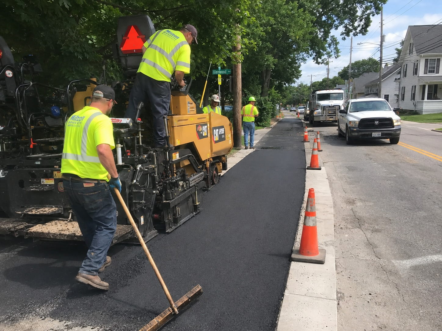 Civil works crew laying fresh asphalt paving along a Perth street with a paving machine and safety cones